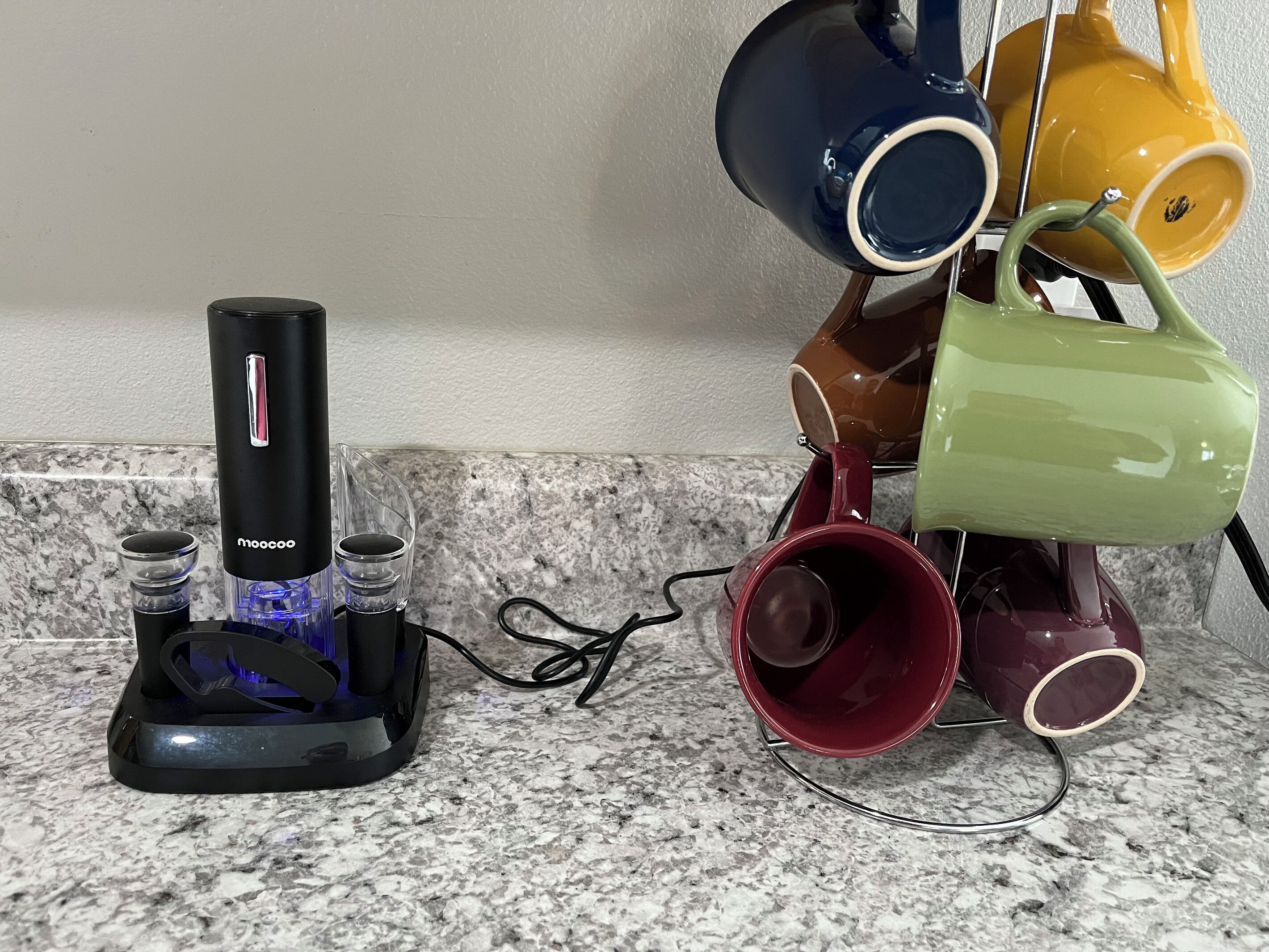 Un bancone cucina con una macchina da caffè, una caraffa di vetro e un espositore per tazze con diverse tazze.