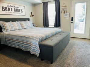 A bedroom with a bed, a bench, a wall sign, a window, and a door.
