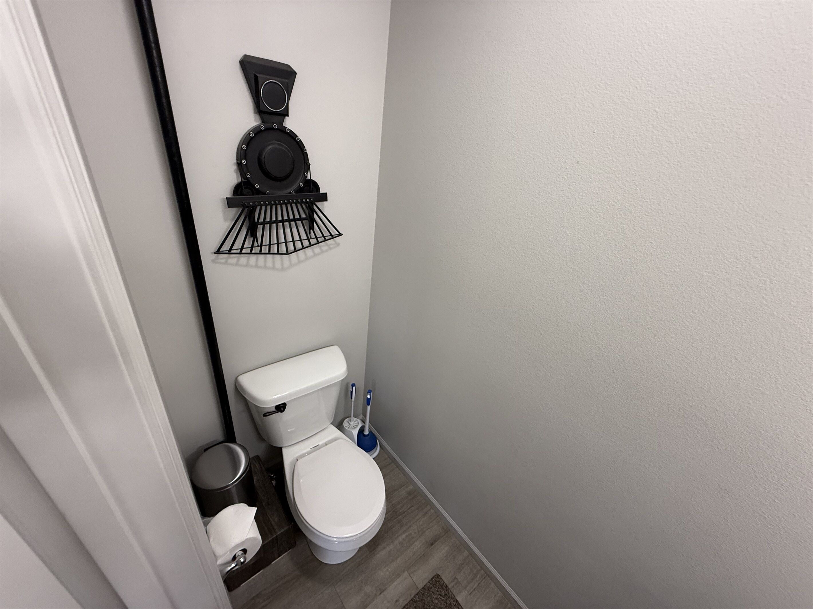 A compact bathroom with a toilet, a wall-mounted toilet paper holder, a small trash bin, and a floor-mounted bidet.