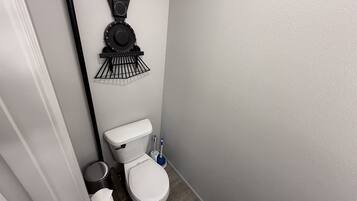 A compact bathroom with a toilet, a wall-mounted toilet paper holder, a small trash bin, and a floor-mounted bidet.