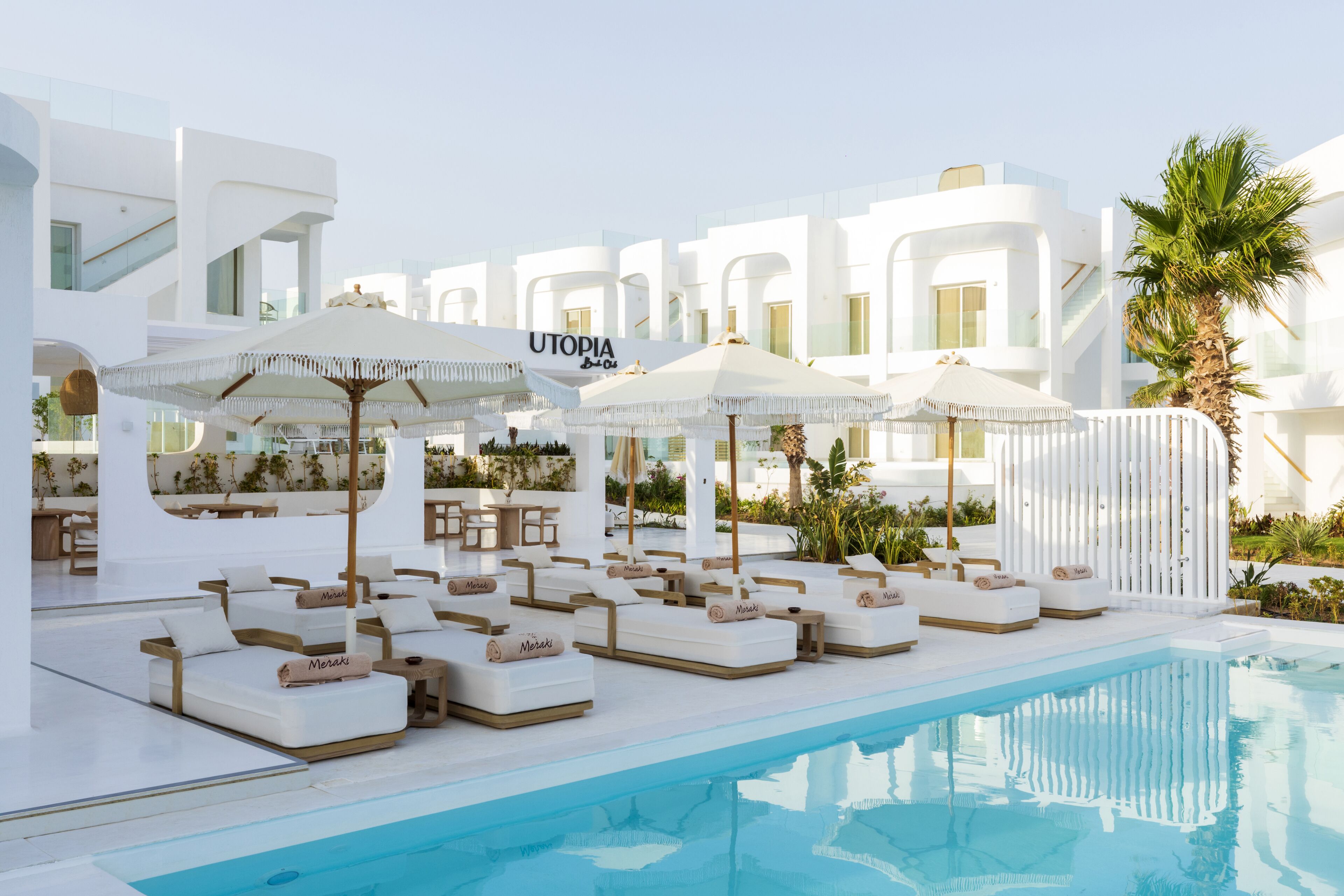 A poolside area with lounge chairs and umbrellas, a clear pool, and a building with the sign 'UTOPIA'.