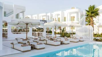 A poolside area with lounge chairs and umbrellas, a clear pool, and a building with the sign 'UTOPIA'.
