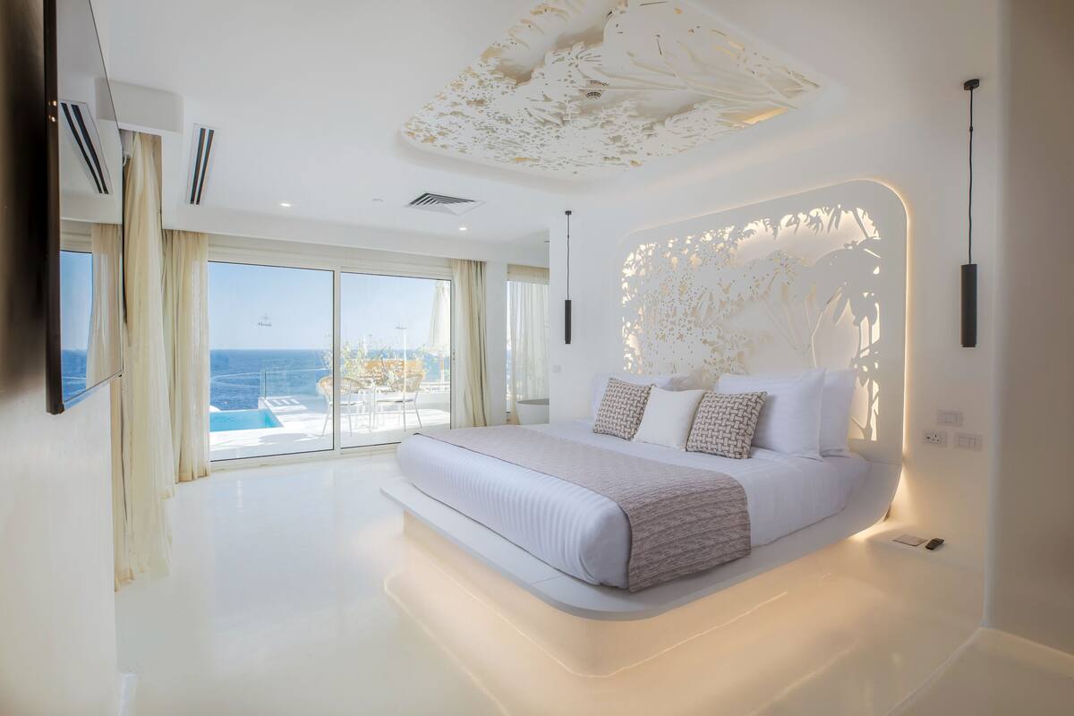 A modern bedroom with a large bed, a view of the sea, and a unique ceiling design.