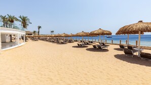A beach with rows of sun loungers and thatched umbrellas, a clear sky, and a boat in the water. - Meraki Sharm El Sheikh Resort (Sharm El Sheikh)