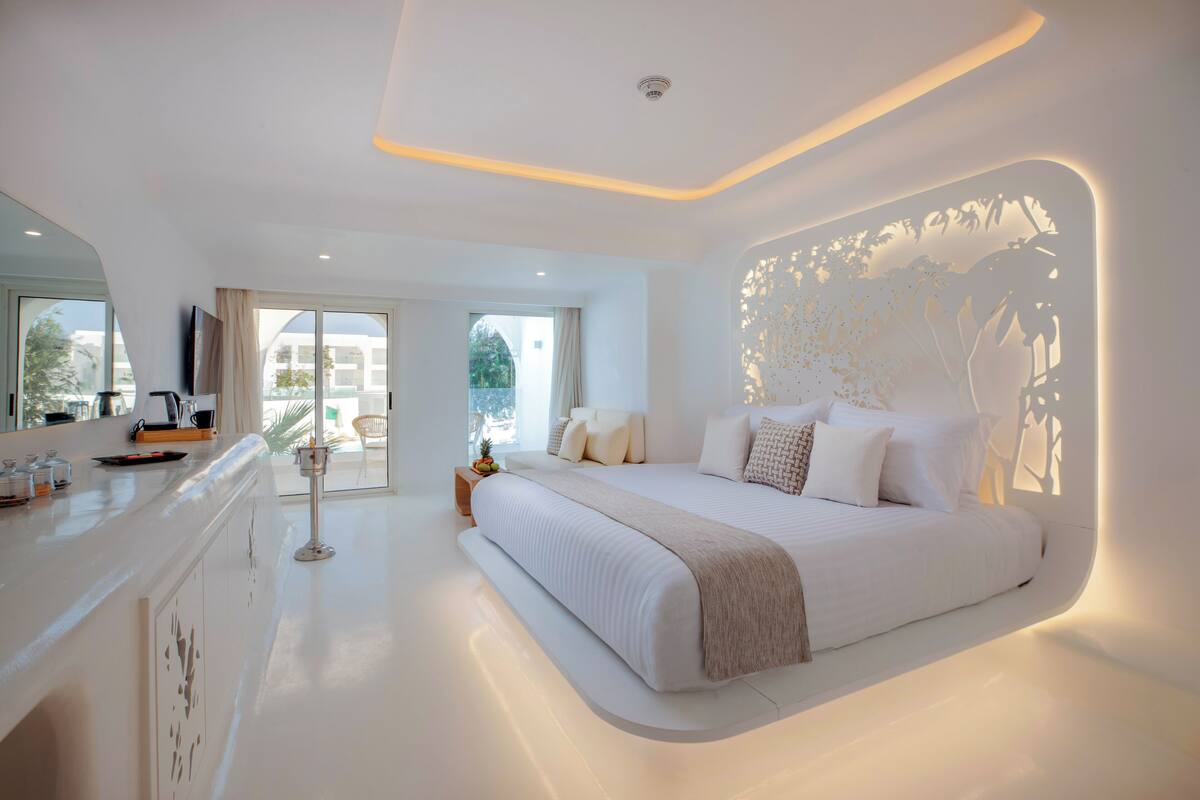A modern bedroom with a large bed, a bedside table, and a view of the outdoors.