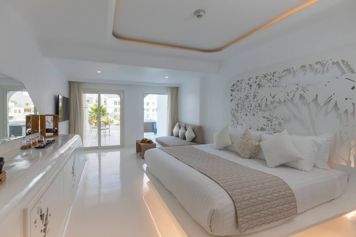 A modern hotel room with a large bed, a vanity with a mirror, and a view of the outside.