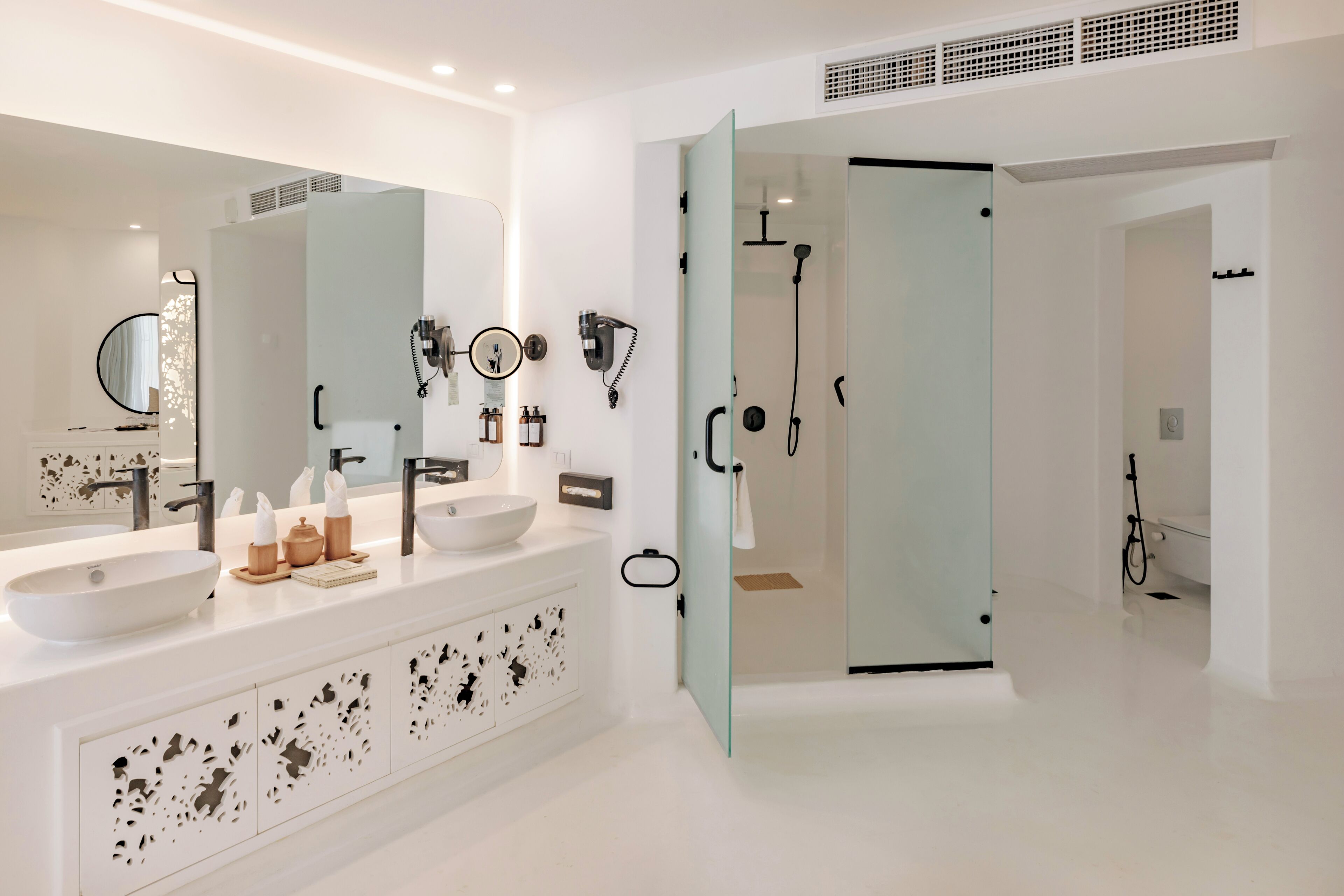 A modern bathroom with two sinks, a large mirror, and a glass-enclosed shower area.