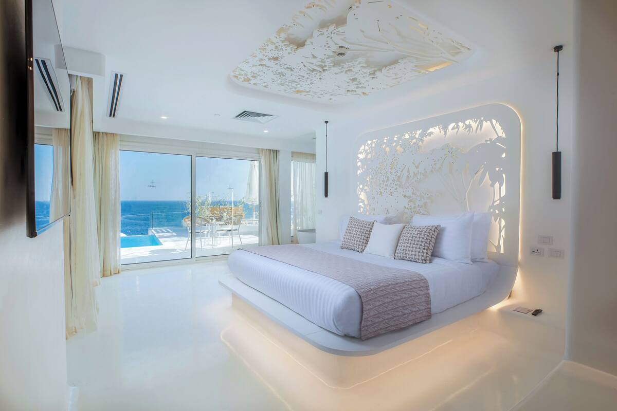 A modern bedroom with a large bed, a view of the sea, and a unique ceiling design.