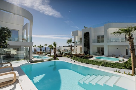 A modern resort with a large infinity pool, multiple swimming pools, and a clear view of the ocean.