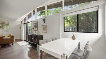 A modern living room with a white dining table, grey chairs, a brown sofa, and a dark wooden cabinet.