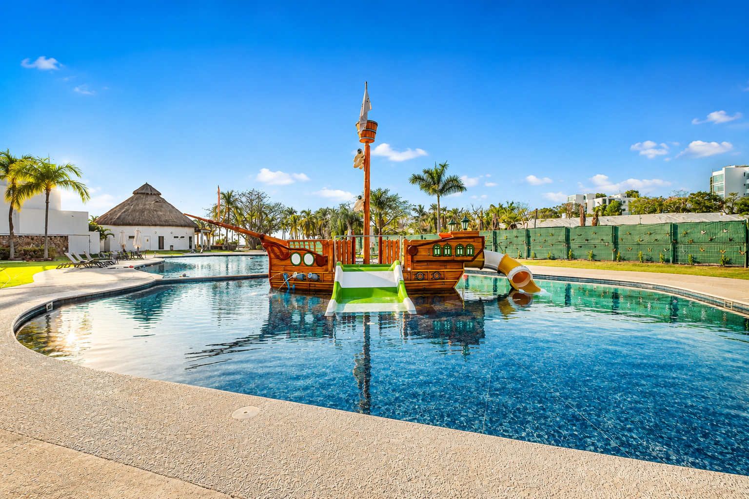 A swimming pool with two wooden ship-shaped structures, a thatched-roof building, and palm trees.