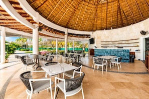 Un área de comedor al aire libre con mesas y sillas, un bar y vistas a la vegetación.
