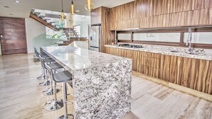 A modern kitchen with a marble island, wooden paneling, and a stainless steel refrigerator.