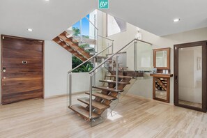 A modern interior with a wooden staircase, a glass door, and a view of greenery outside.