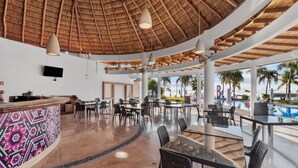 A spacious outdoor dining area with a thatched roof, tables, chairs, and a poolside view.