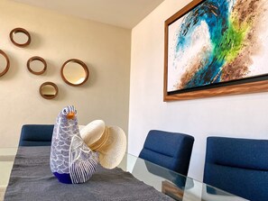 Una habitación moderna con una mesa de vidrio, sillas tapizadas en azul, un adorno en la pared y un objeto decorativo sobre la mesa.