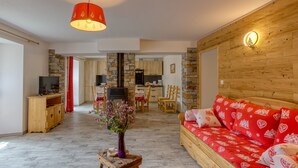 Un salon moderne avec un canapé rouge, une table basse en bois surmontée d’un vase, et une cuisine en arrière-plan.