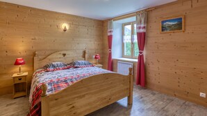 Une chambre à coucher aux murs lambrissés, avec un lit, des lampes de chevet, une fenêtre avec des rideaux et un luminaire fixé au mur.