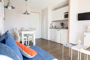 Uma sala de estar moderna com sofá, mesa de jantar e cozinha com armários brancos e micro-ondas.