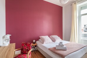 Une chambre d’hôtel avec un lit, une chaise, une petite table et une fenêtre avec des rideaux.