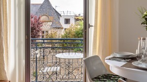 Un balcon orné d’une balustrade en fer forgé, une table dressée pour le dîner et une vue sur un bâtiment en pierre doté d’un toit en flèche.