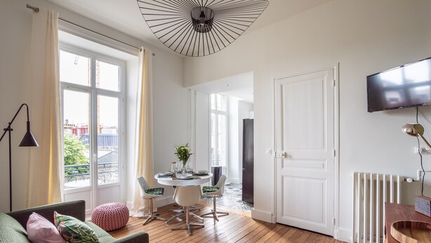 Un salon moderne avec un plancher en bois, un canapé vert agrémenté de coussins, une table à manger avec des chaises et un téléviseur fixé au mur.