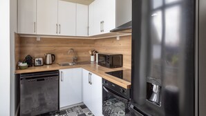 Une cuisine moderne avec des meubles blancs, un réfrigérateur en acier inoxydable, un four à micro-ondes, un lave-vaisselle et un plan de travail en bois.