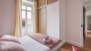 Une chambre d’hôtel avec un lit, une fenêtre avec des rideaux, une armoire en bois et une porte donnant sur une autre pièce.