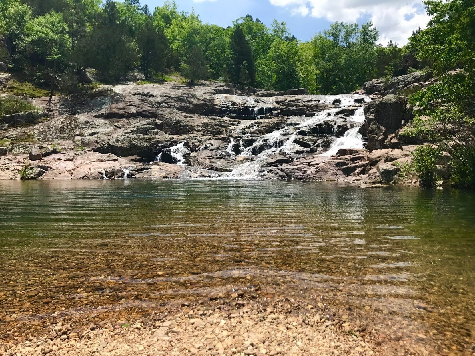 Een natuurlandschap met helder water, rotsachtig terrein en een waterval.