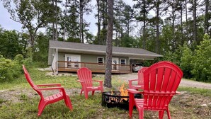 Une cabane dotée d’une terrasse, entourée d’arbres, et d’un espace extérieur aménagé avec un foyer.