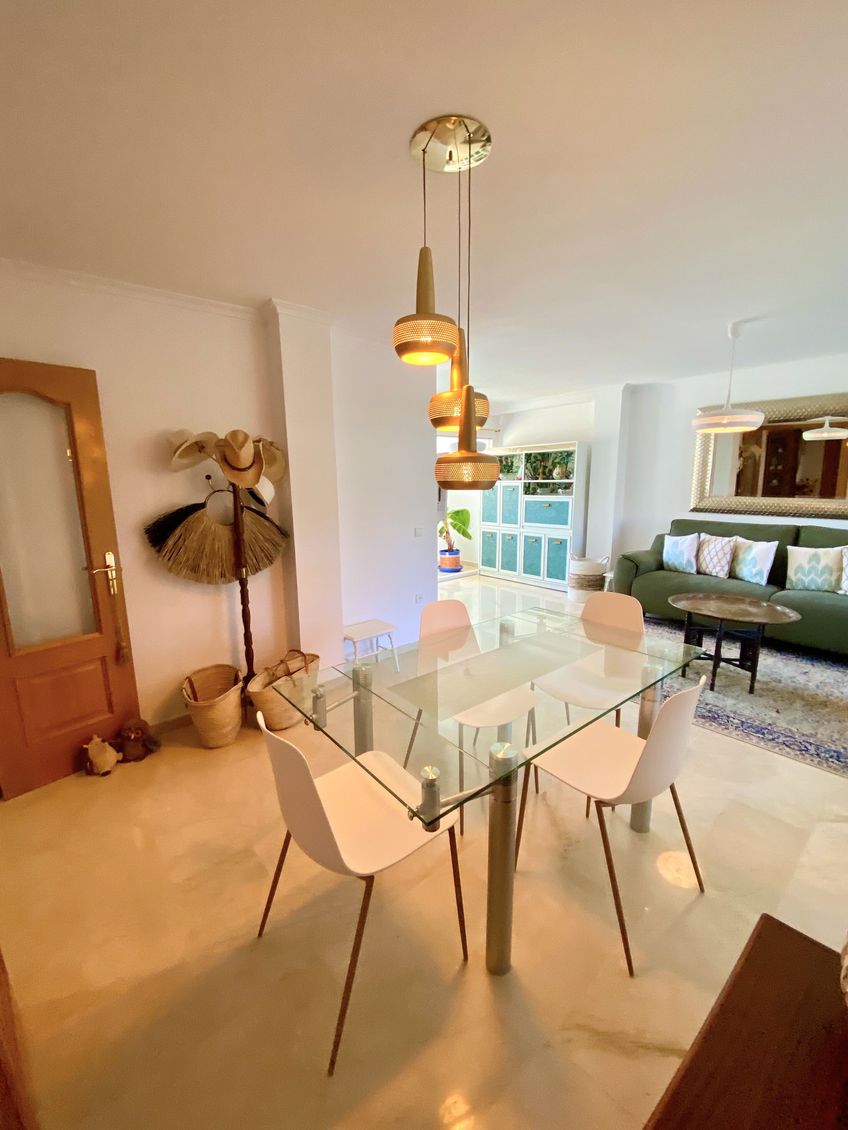 Ein modernes Wohnzimmer mit einem Glastisch, weißen Stühlen, einem grünen Sofa und einer Deckenleuchte.