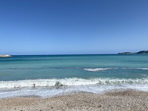 A pebbled beach with clear turquoise water and gentle waves.