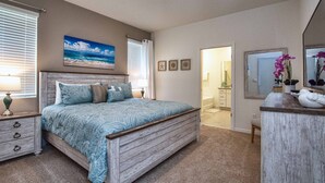 A bedroom with a bed, a dresser, a mirror, and a painting of the ocean.