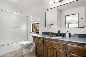 Une salle de bain moderne équipée d’une douche, de toilettes, d’un meuble-lavabo avec un évier et d’un grand miroir.