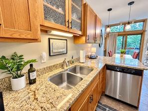 A kitchen with granite countertops, stainless steel appliances, wooden cabinets, and a window with a view.