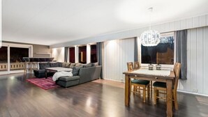A spacious living room with a large sofa, a dining table with chairs, and a chandelier.