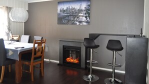 A dining area with a fireplace, a cityscape painting, and two bar stools.