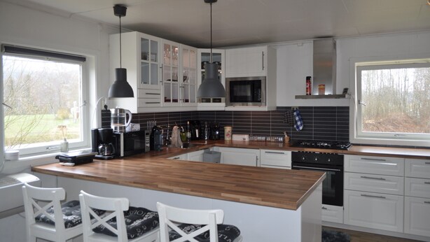 A modern kitchen with white cabinets, a wooden island, and a large window.