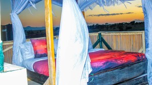 Un lit à baldaquin, une tête de lit en bois et une vue sur le coucher de soleil.