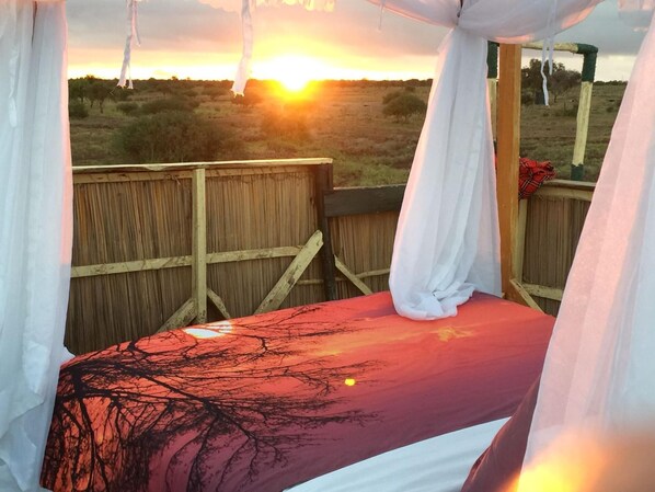 A bed with a red and black tree pattern, a wooden fence, and a sunset view.