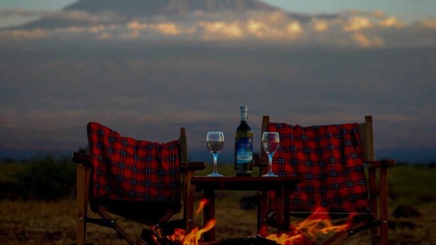 Deux fauteuils recouverts d’un tissu à carreaux, placés face à une table sur laquelle se trouvent une bouteille et des verres, le tout sur fond de paysage montagneux.