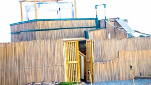 Une construction rustique en bois, dotée d’une porte d’entrée centrale, d’un petit jardin et d’un château d’eau.