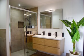 Features a sleek bathroom with a large mirror, glass shower enclosure, and a wooden vanity.
