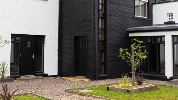 A modern two-story house with a black exterior and white walls, featuring a driveway and a small garden area with plants. - Bushmills Hostel (Bushmills)