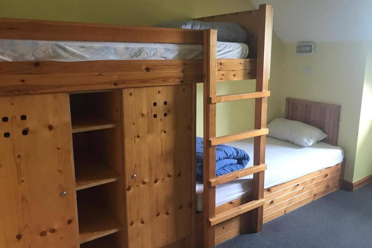A bunk bed with a ladder, a small shelf unit, and a single bed with pillows.