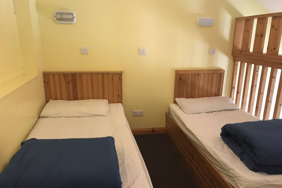 Two single beds with wooden headboards in a room with yellow walls and a slatted wooden partition.