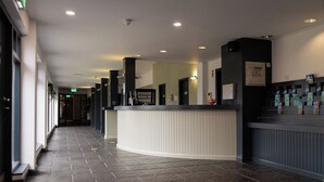 A hotel reception area with a curved reception desk, a security camera, and a wall-mounted information board. - Bushmills Hostel (Bushmills)