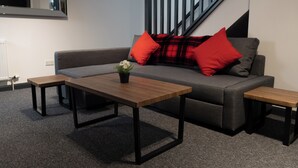 A modern living room with a grey sofa, two wooden side tables, and red cushions. - Bushmills Hostel (Bushmills)