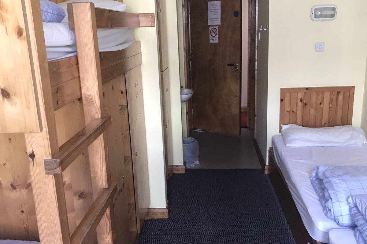 A narrow hallway with bunk beds on either side, a door at the end, and a small window with a polka dot curtain.
