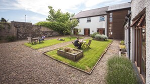 A courtyard with a gravel path, two seating areas with tables and chairs, a wooden planter box, and a stone wall. - Bushmills Hostel (Bushmills)
